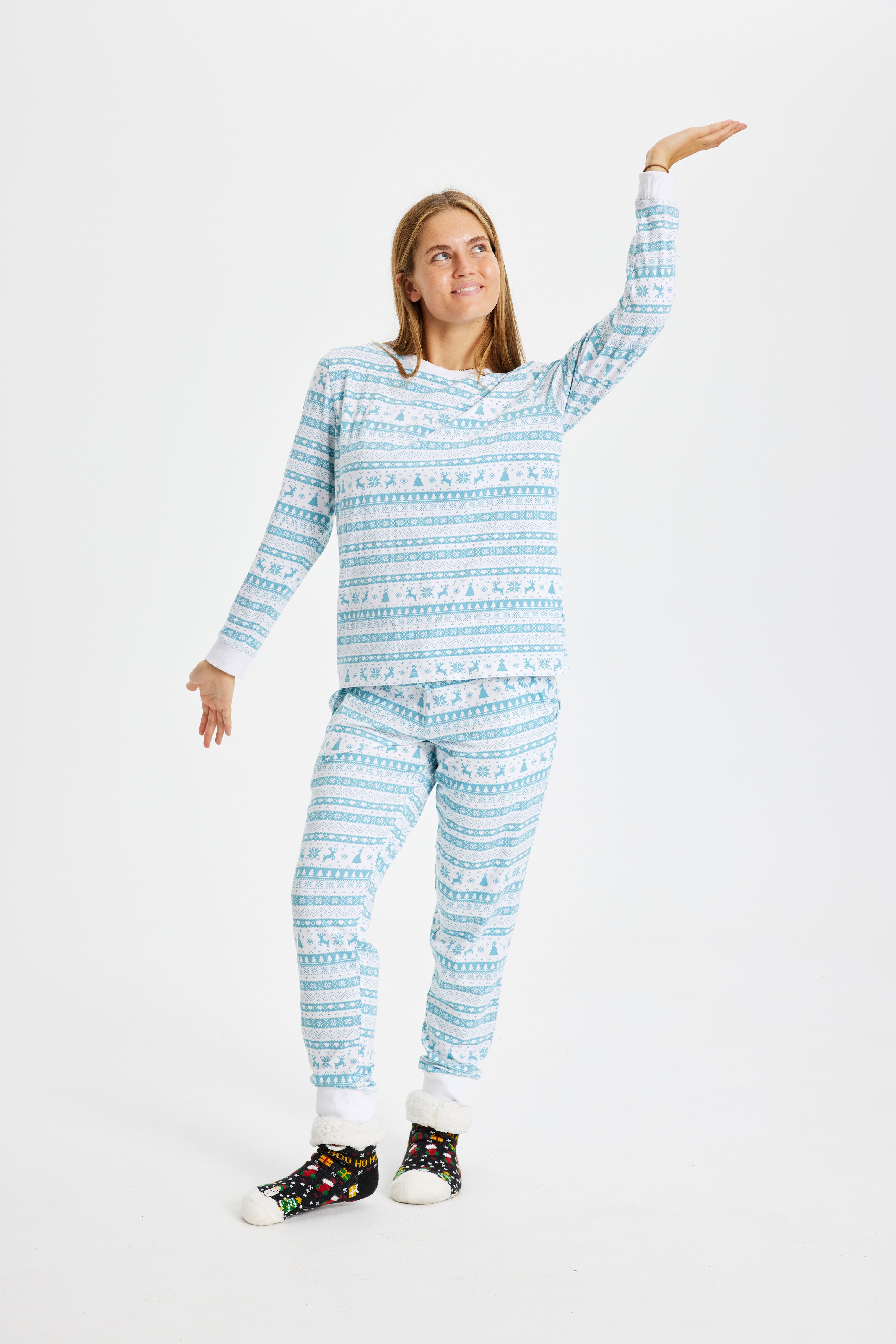 En kvinne med hendene i været iført en blå julepyjamas med julemønster.